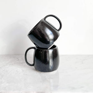 A set of 2 black stoneware ceramic mugs, stacked.