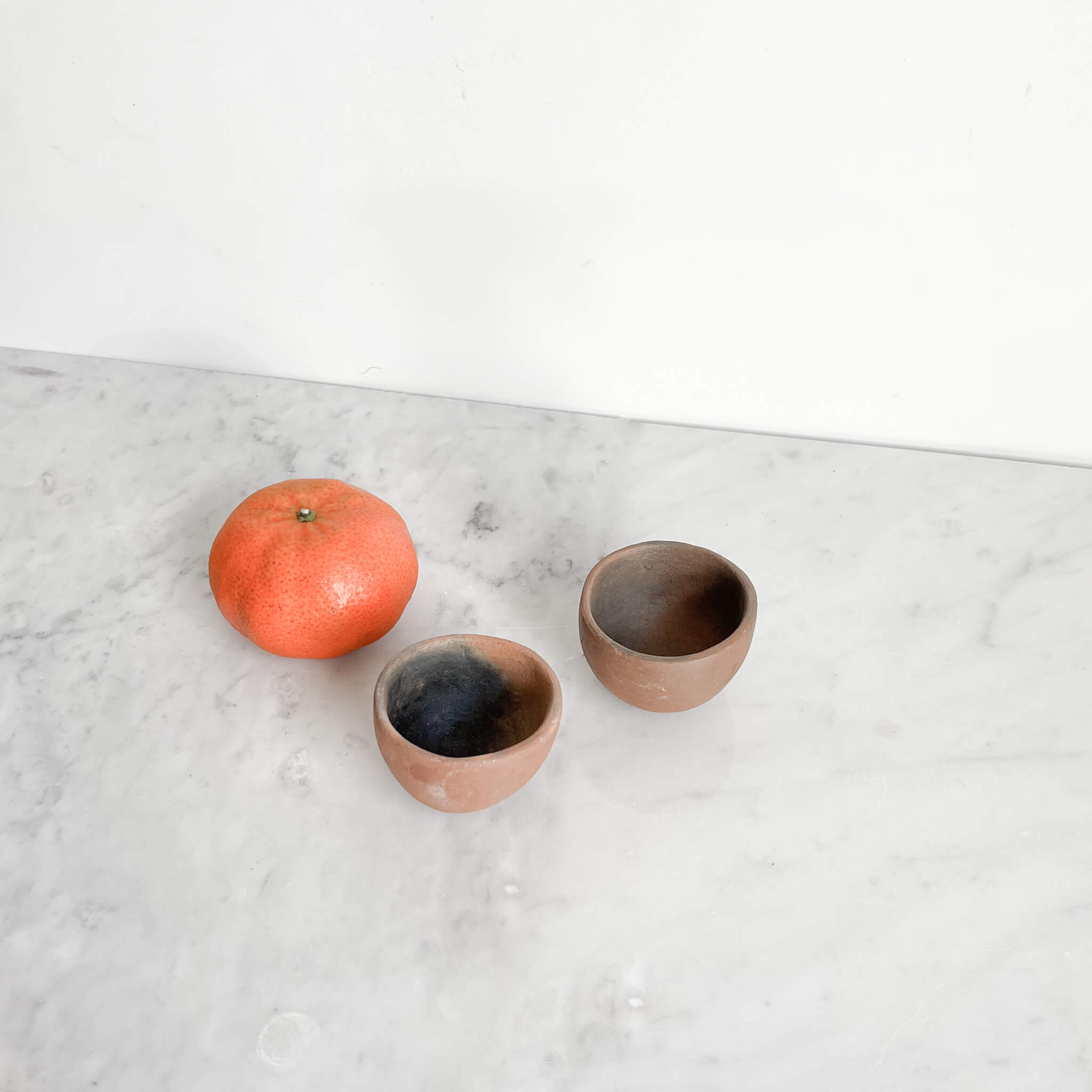 A set of 2 clay mezcal copita cups next to a small orange.