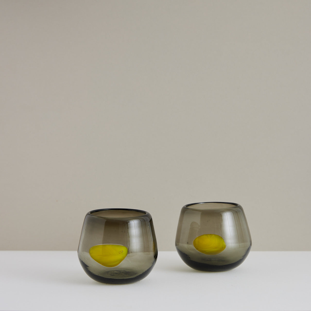 A pair of smoky gray handblown cocktail glasses with a yellow dot made in Mexico.