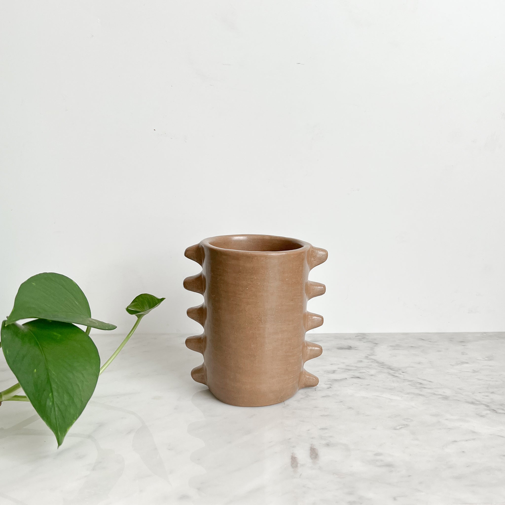A spiky clay mug made in Mexico on a white marble counter.