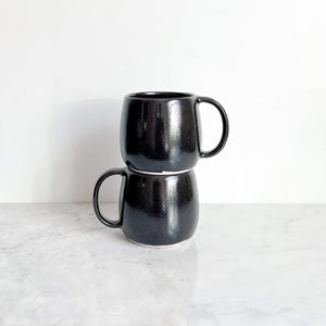 A set of two stacked stoneware ceramic mugs in black.