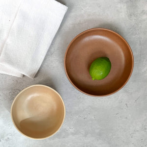 Set of stoneware bowls in sandy ivory and rust terracotta on a concrete table next to a white cotton napkin.