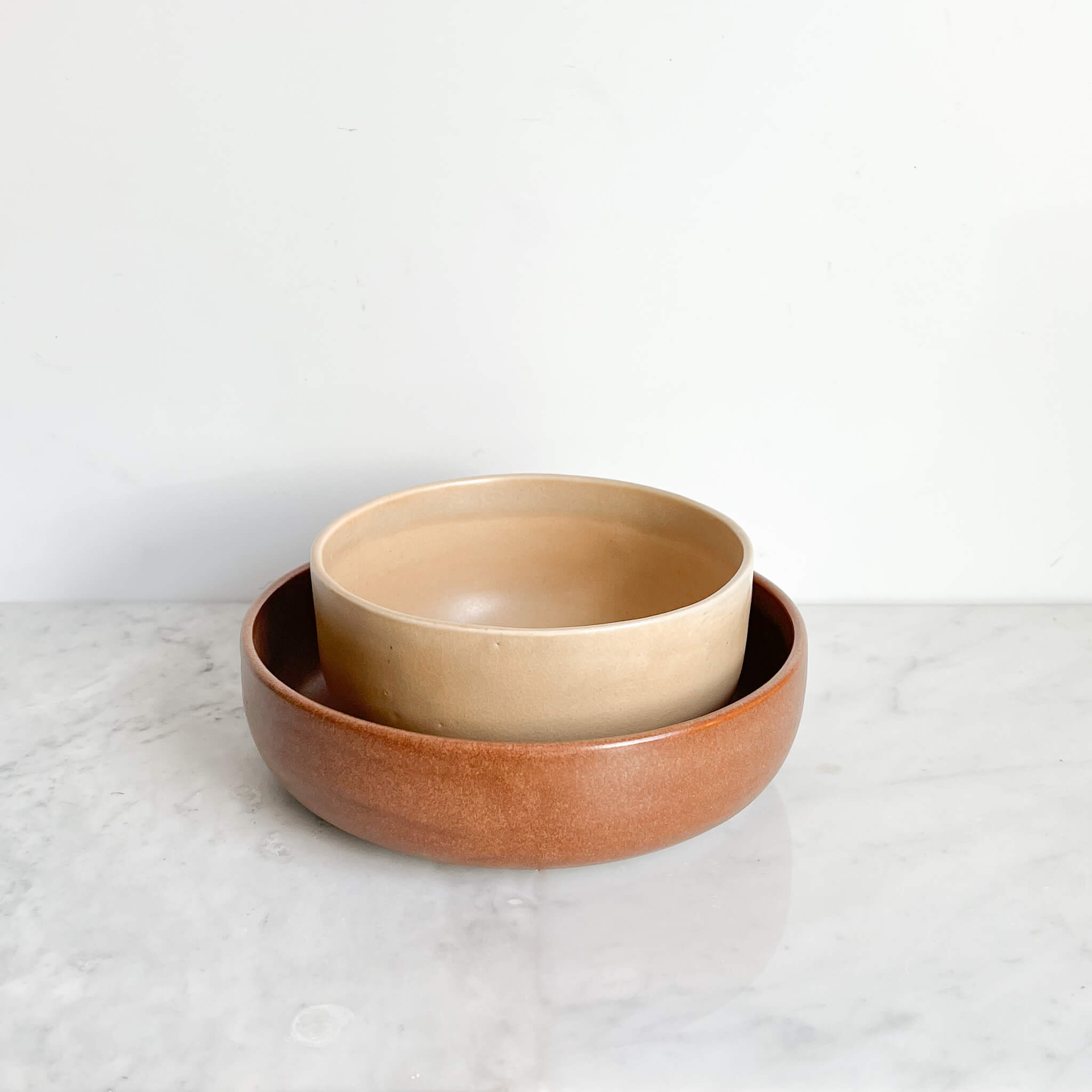 A set of stacked stoneware serving bowls on a white marble counter.
