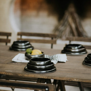 An outdoor table set with black stoneware dining dishes.
