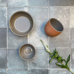 A collection of 3 terracotta bowls with gray glaze on gray concrete tile.
