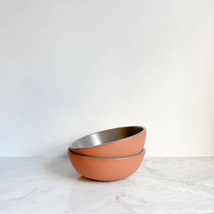 A set of two terracotta and gray glazed cereal bowls on a white marble counter.