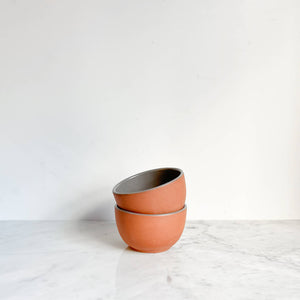 A set of 2 terracotta bowls with gray interior glaze stacked on a marble counter.