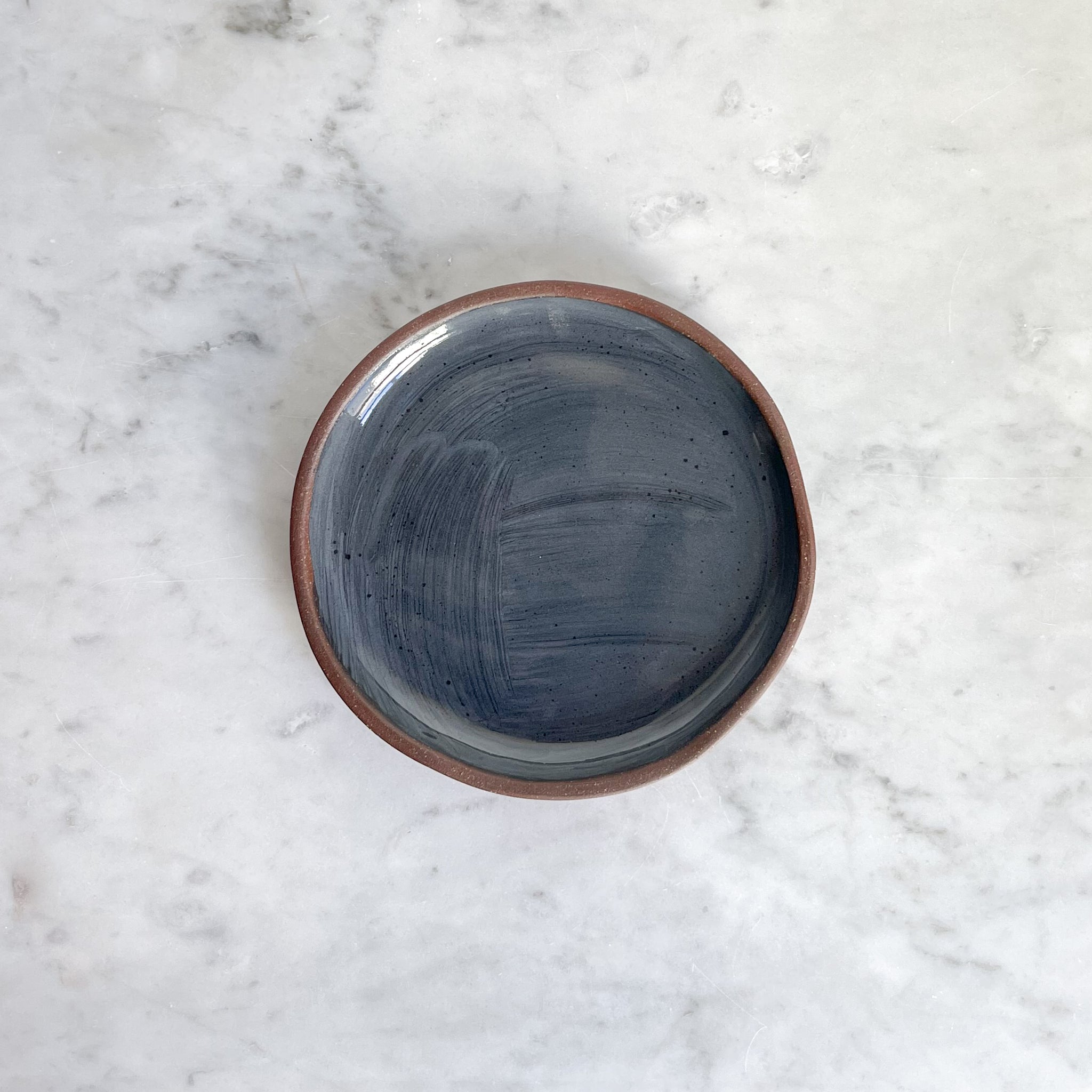 A single small ceramic plate with gray glaze on a marble counter.