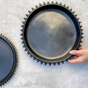 A deep, black clay serving tray held in a hand.