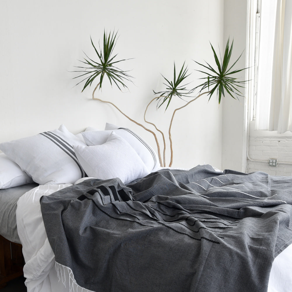 A black cotton coverlet draped over a cozy bed in a bright room.