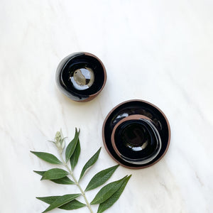 A set of black dipped terra-cotta ceramic mugs with a plate.