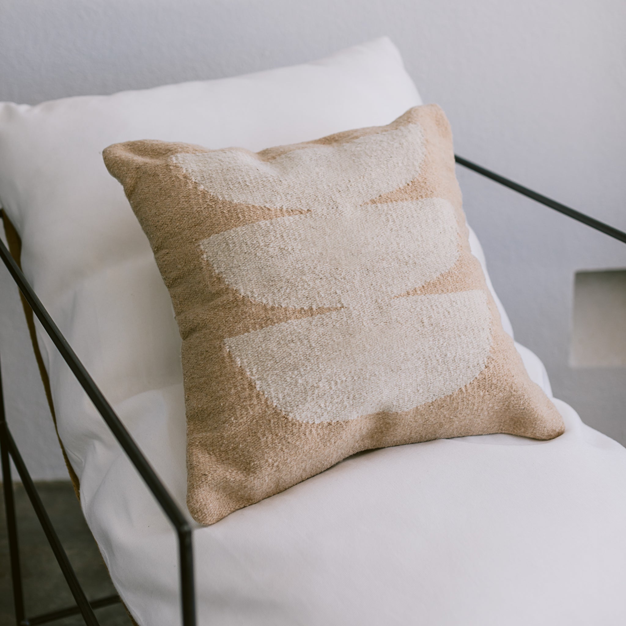 A wool ivory and beige-colored throw pillow on a white chair.