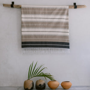 A cotton throw folded and hung on a wall hanger with ceramic vases on the floor below.