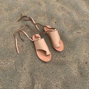 A pair of nude colored leather sandals on a beach.