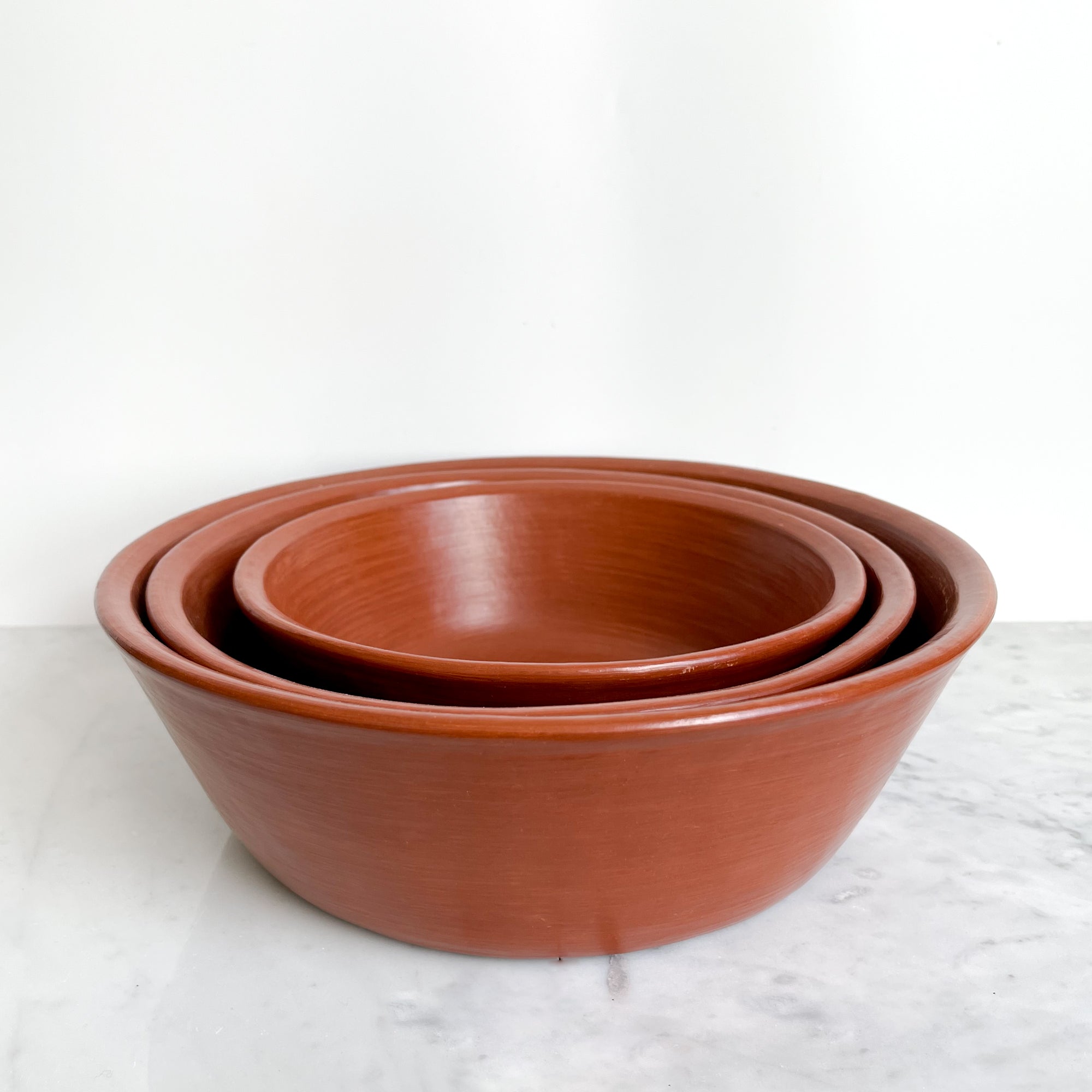 A set of nested red clay serving bowls on a marble counter.