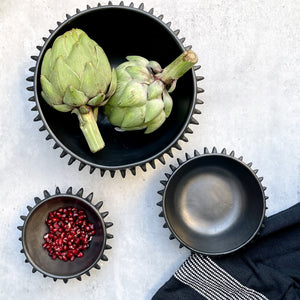 Three Oaxaca black clay bowls with artichokes, pomegranate seeds and a black and white hand towel.