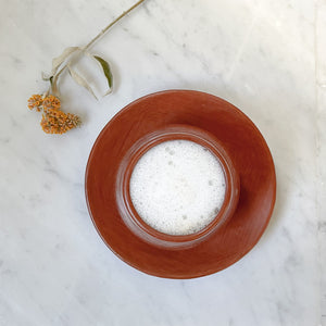 A stemless mug and plate set made in Oaxaca with red clay on a white marble counter.