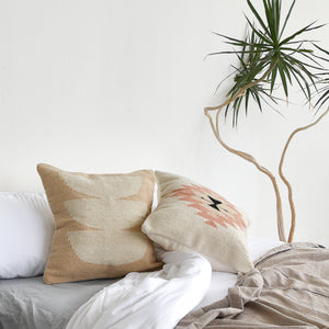A set of wool Oaxaca throw pillows on a cozy bed with a yucca plant alongside.