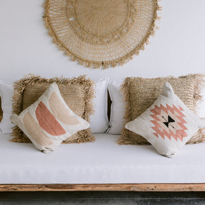 A set of wool throw pillows arranged on a white couch with handwoven palm accents.