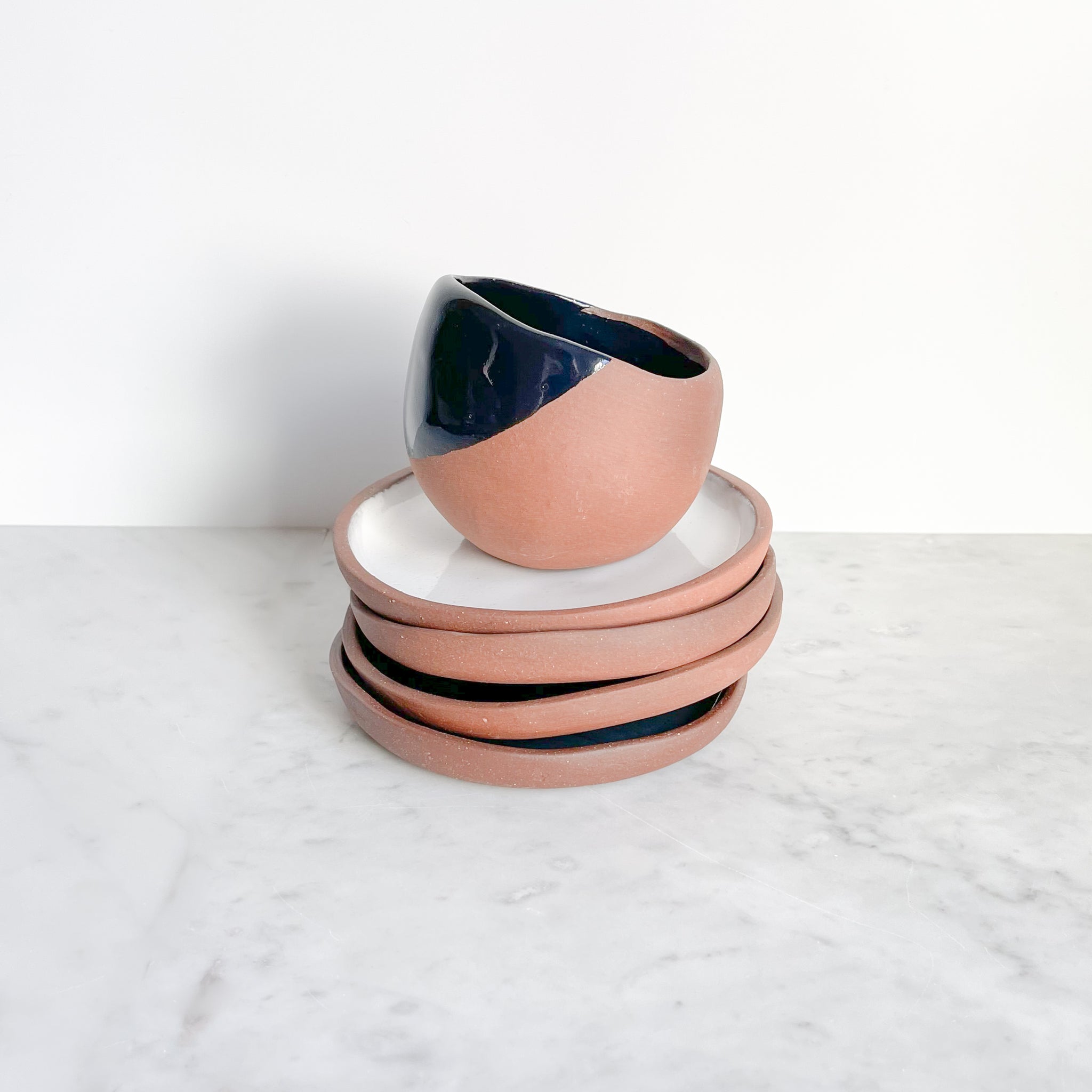 A black dipped terra-cotta mug stacked on white terra-cotta plates on a marble counter