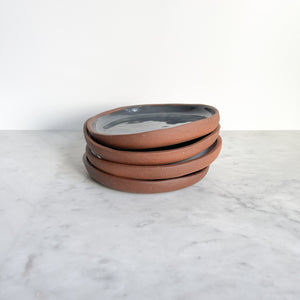 A set of four ceramic gray plates stacked on a marble counter.