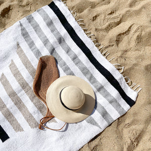 The Artesanal's San Borja Mexican blanket on a beach with a palm hat and Chiapas fiber bag.