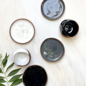 A set of small ceramic plates with coordinating mugs on a white marble counter.