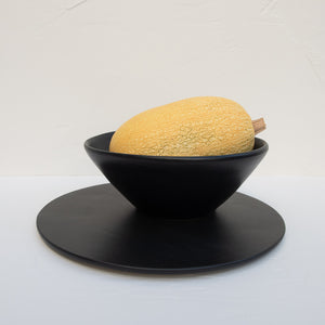 A matte-black stoneware serving platter and serving bowl (holding a large squash).