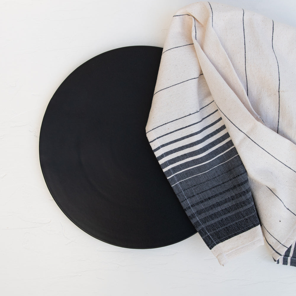 A matte black stoneware serving platter with a cotton Oaxaca hand towel.