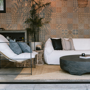 The living room in a modern beach house includes an intricately tiled wall, a plush white couch with heirloom throw pillows, a charcoal gray coffee table and a metal Crofthouse chair with suede throw pillows.