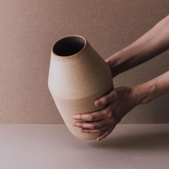 A terra-cotta ceramic vase being held in two hands.