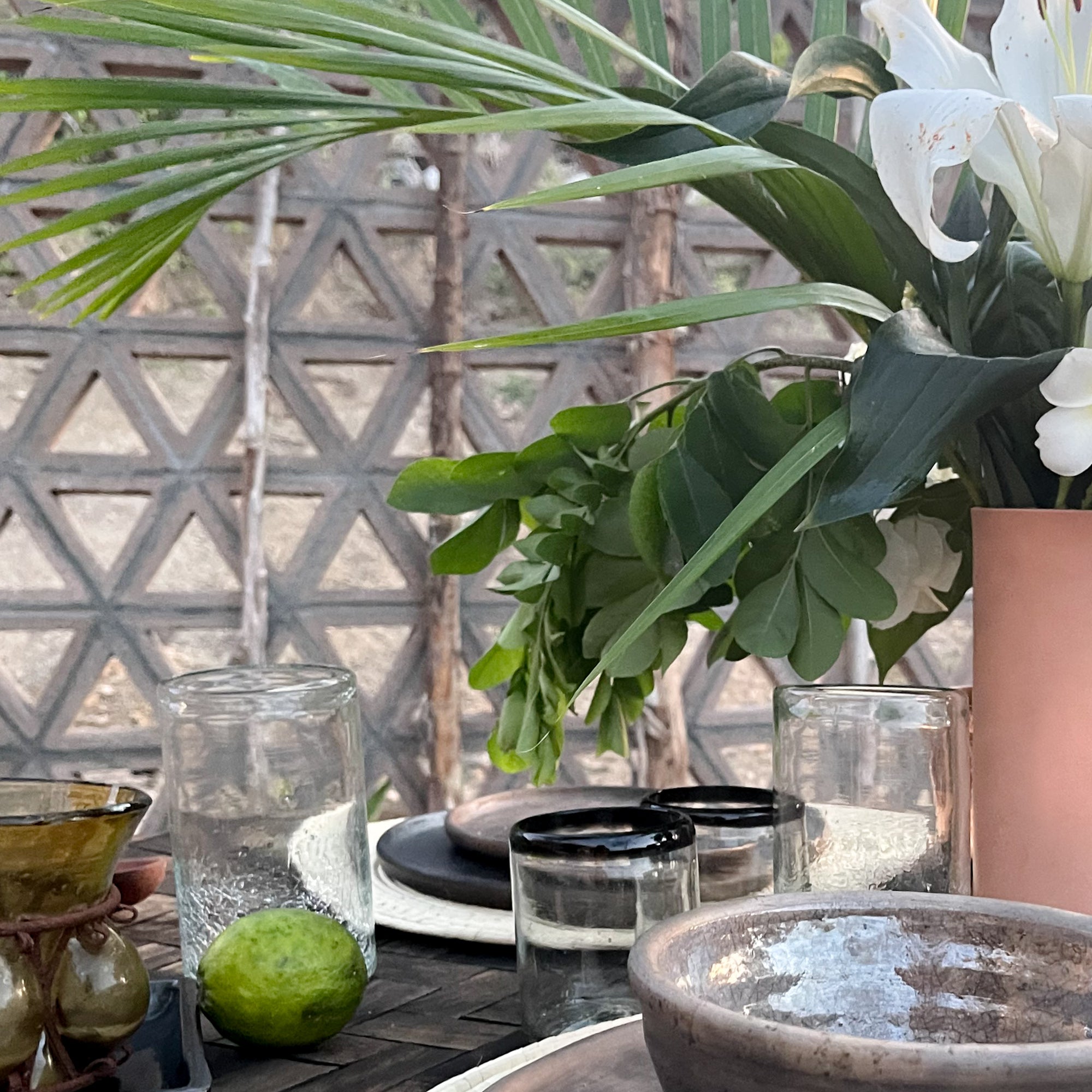 A table set with black rimmed glassware, and Oaxaca clay dishes, a vase with flowers and limes.