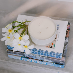 A three wick white ceramic candle on a stack of surf books.