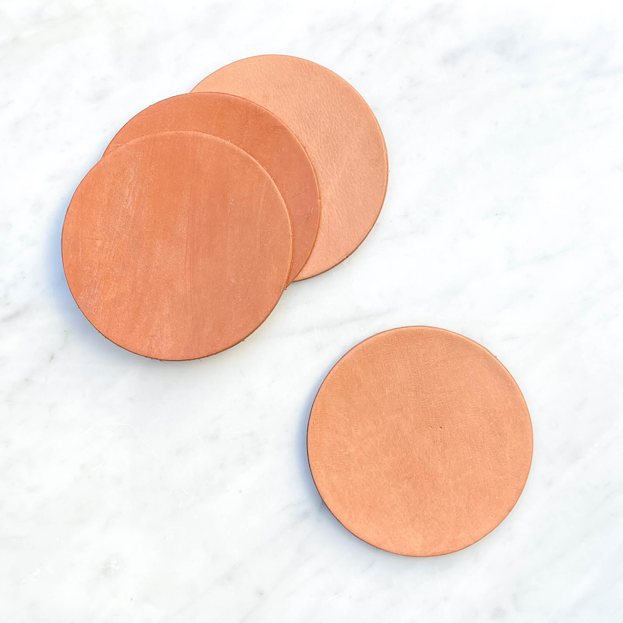 A set of 4 vaquero leather coasters on a marble counter.