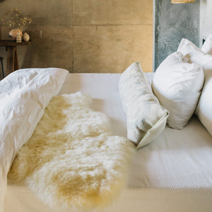A 2x4 foot ivory sheepskin throw on a white bed as a blanket.