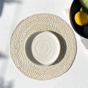 A white stoneware salad plate on a handwoven palm placemat.