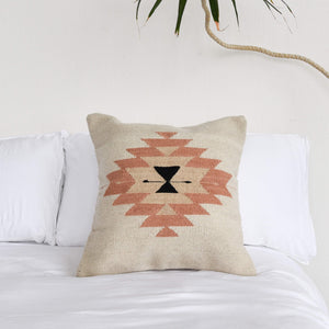 Details of the design on a Zapotec wool throw pillow on a white bed.